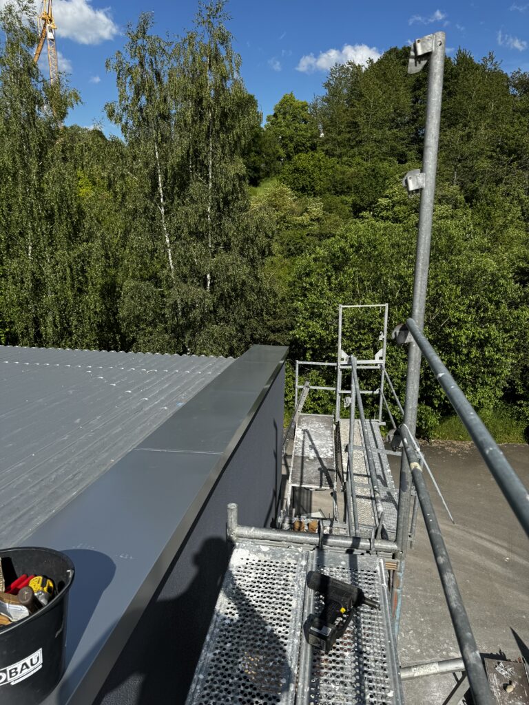 Flachdach mit Attikaverkleidung aus Metall und Gerüst während der Arbeiten