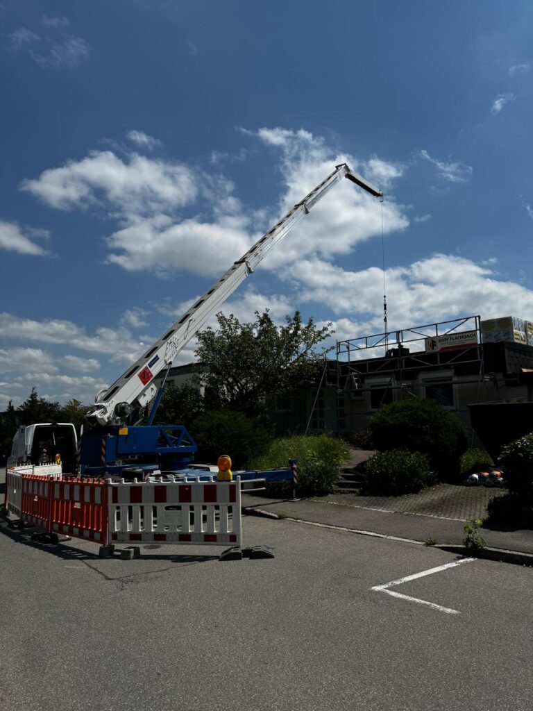 Autokran hebt Material für Dacharbeiten auf die Baustelle